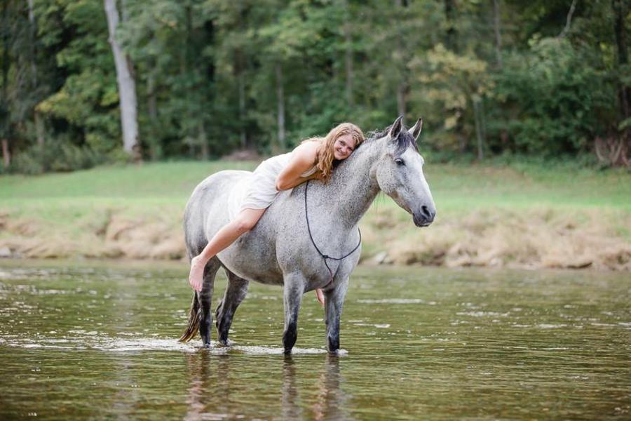 Parelli Instruktorin Anais Zimmermann liegt auf Ihrem Pferd welches im Wasser steht. 